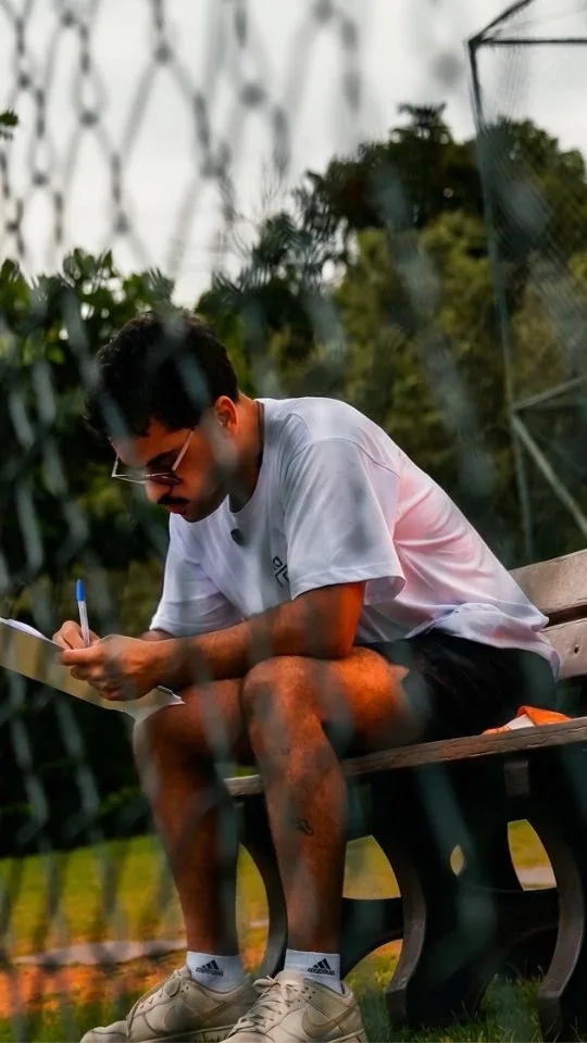 Pessoa com camiseta do NaTrave faz anotações em papel na lateral do campo