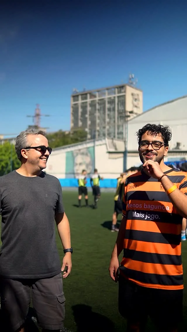 Duas pessoas conversam no campo, uma delas com microfone e camiseta do NaTrave